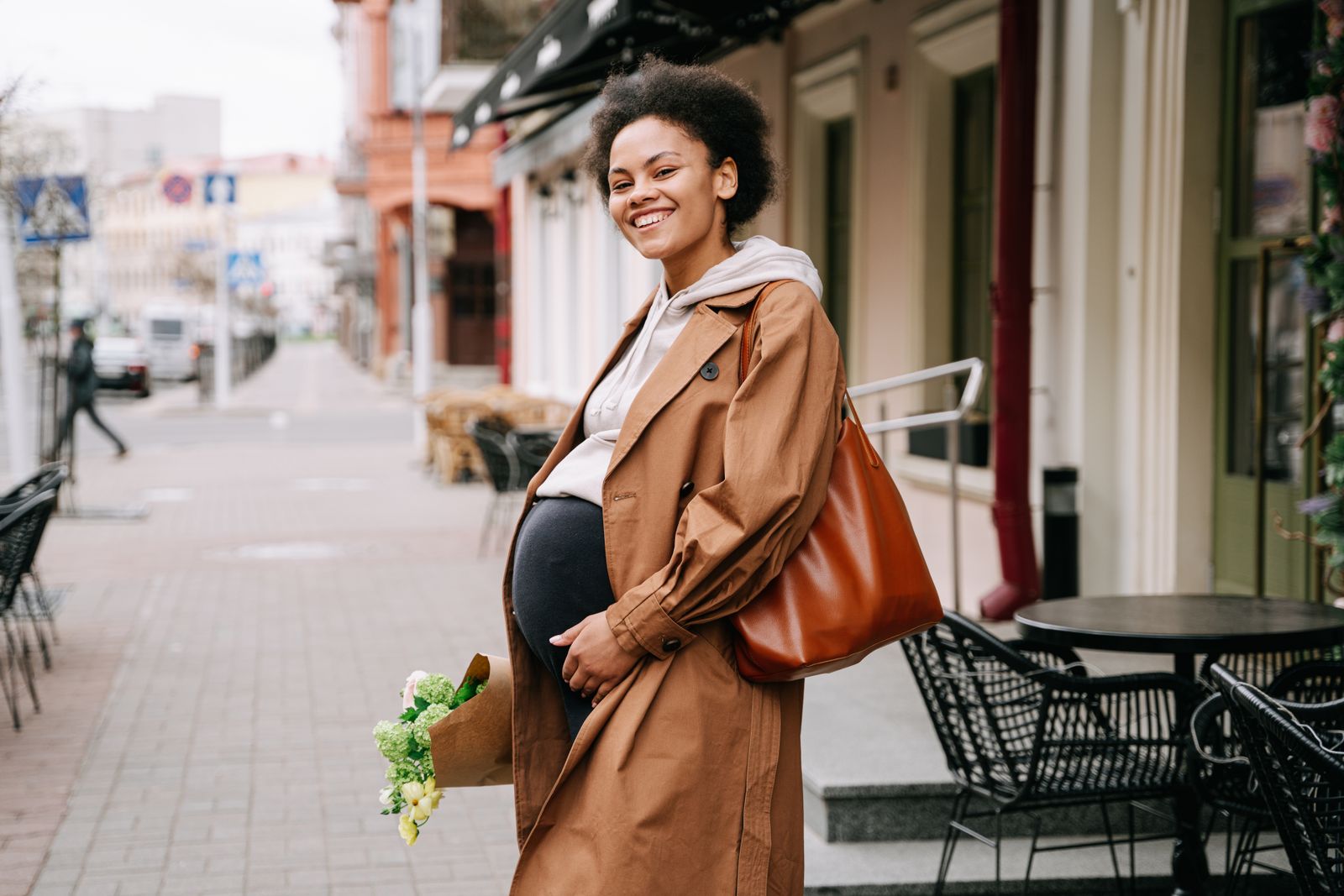 Smiling pregnant woman in a brown coat on a Lisbon street, on her way to a tile painting workshop